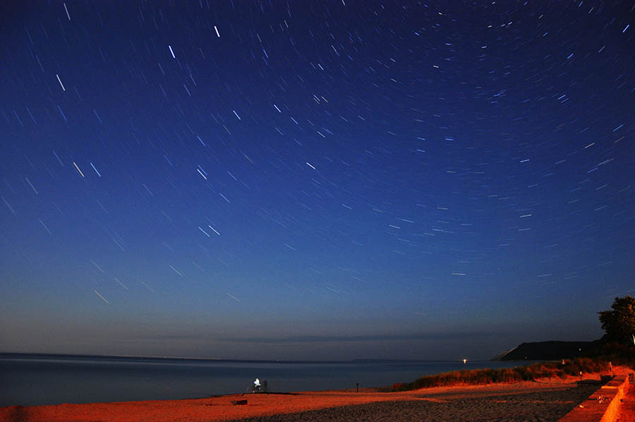 Time exposure of stars above a Lake Michigan beach.